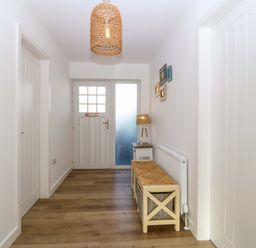 A hallway with wooden flooring a white entrance door a bench with baskets and a lamp on a side table at Awel-Y-Mor Trearddur Bay
