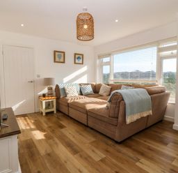 A living room with a brown sectional sofa near a window with blinds and a television on a stand at Awel-Y-Mor in Trearddur Bay