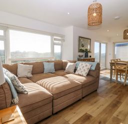 A living room with a brown sectional sofa and dining table in the background at Awel-Y-Mor in Trearddur Bay