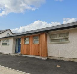 The exterior of a single-story house with a blue door and windows surrounded by wood paneling at Awel-Y-Mor in Trearddur Bay