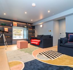 A living room with two blue couches a colorful rug a telescope and a built in shelving unit at Mavericks Wave in St Agnes