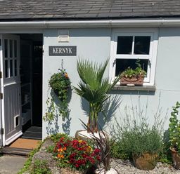 The exterior of a white house with an open door a window flower pots and a sign that says Kernyk at Kernyk Carn Brea near Pool