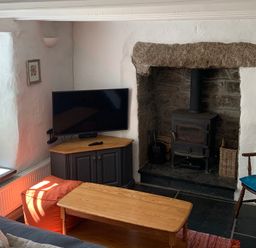 A living room with a wood stove fireplace television on a cabinet wooden coffee table and chair with cushions at Kernyk in Carn Brea near Pool