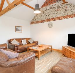 A living room with brown leather sofas a wooden coffee table a television on a wooden cabinet and a clock on the wall at The Old Dairy in Tittleshall near Brisley