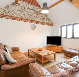 A living room with brown leather sofas a wooden coffee table and a television at The Old Dairy in Tittleshall near Brisley