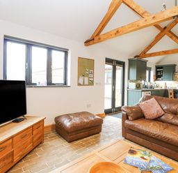 A living room with a brown leather sofa and ottoman a wooden TV stand with a television and a wooden coffee table at The Old Dairy in Tittleshall near Brisley