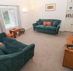 A living room with two teal sofas a television on a wooden stand and a window with curtains at Wood Cottage in Solva