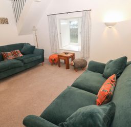 A living room with two green sofas two small wooden tables and animal shaped stools at Wood Cottage in Solva