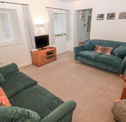 A living room with green sofas a wooden TV stand and small wall pictures at Wood Cottage in Solva