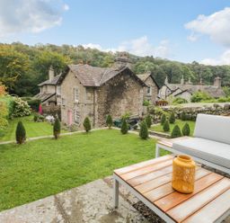 A garden with a sofa and table and stone houses in the background at Pear Tree Cottage in Grange-Over-Sands