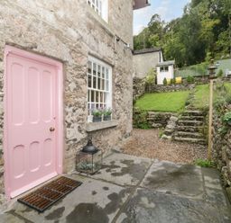 A stone house with a pink door and window with flowers outside a garden with stone steps and green grass at Pear Tree Cottage in Grange-Over-Sands