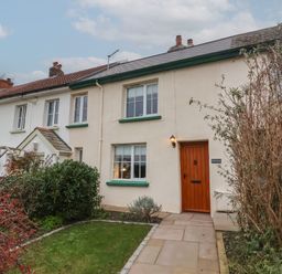 A row of connected houses with white walls green window frames a wooden front door and a small garden path at Sunnymead in Bickington near Barnstaple