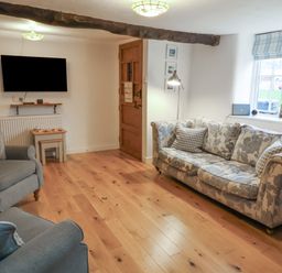A living room with a patterned sofa two armchairs a wall mounted television wooden door and wood flooring at Sunnymead in Bickington near Barnstaple