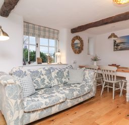 A living room with a floral sofa a dining table with chairs and a window with checkered curtains at Sunnymead Bickington near Barnstaple