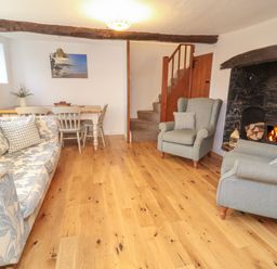 A living room with a fireplace wooden floor a sofa armchairs a dining table chairs and a staircase at Sunnymead in Bickington near Barnstaple