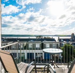 A balcony with two chairs and a glass table overlooking rooftops and water at Slipway 14 in Rock