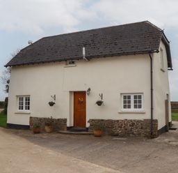 A small cream colored house with a dark roof and wooden door at Cherryblossom Cottage in Winkleigh