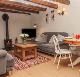 A living room with a wood burner tv grey sofas wooden coffee table white distressed chairs and a round dining table at Cherryblossom Cottage in Winkleigh