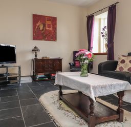 A living room with a coffee table with flowers a sofa a TV on a stand and a window with purple curtains at Ty Llugwy in Capel Curig near Betws-Y-Coed