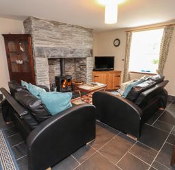 A living room with two black leather sofas and a stone fireplace with a wood stove at Ty Siabod in Capel Curig near Betws-Y-Coed