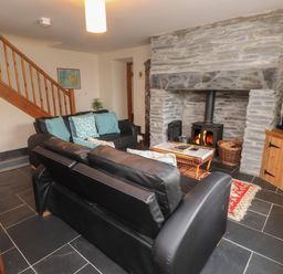 A living room with black leather sofas a stone fireplace a wooden cabinet and staircase at Ty Siabod in Capel Curig near Betws-Y-Coed