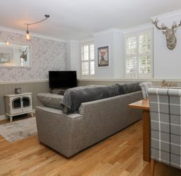 A living room with a gray sofa a television a dining table with plaid chairs and a mounted deer head at 1 Boarbank Farm in Allithwaite near Cartmel