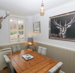 A dining room with a wooden table and four plaid chairs with a deer head wall mount and a large deer painting at 1 Boarbank Farm in Allithwaite near Cartmel