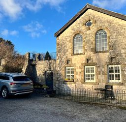 An exterior view of a stone building with arched windows a parked silver car and a small fenced patio with a table and chair at 1 Boarbank Farm Allithwaite near Cartmel