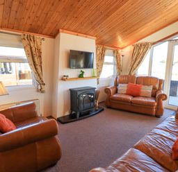 A living room with leather sofas a wall mounted TV and glass doors at Kellet Lodge Lakeside 26 Dock Acres near Carnforth