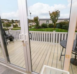 A view of a wooden patio with a round table and umbrella and chairs outside sliding glass doors at 117 Crosswinds Hillway near Bembridge