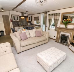 A living room with beige sofas and an ottoman near a fireplace and windows at 117 Crosswinds Hillway near Bembridge