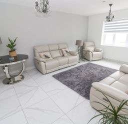 A living room with beige leather sofas a gray rug round table with a plant and lamps at Golygfa Hafan in Little Haven