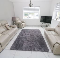 A living room with beige leather sofas armchair a gray rug tiled floor and a TV on a glass stand at Golygfa Hafan in Little Haven