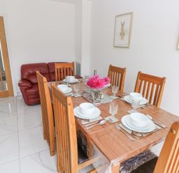 A dining room with a wooden table set for six and a red sofa in the corner at Golygfa Hafan in Little Haven