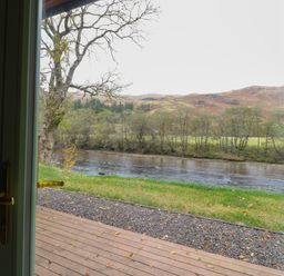 A view of a river trees and hills from a wooden deck outside a house at Bradan Lodge in Dalmally
