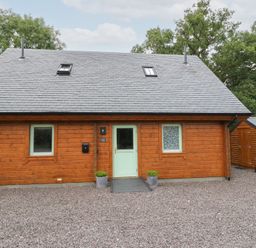A wooden house with a gravel area at Bradan Lodge in Dalmally