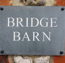 A stone wall with a mounted sign reading Bridge Barn at Bridge Barn in Sidestrand near Overstrand