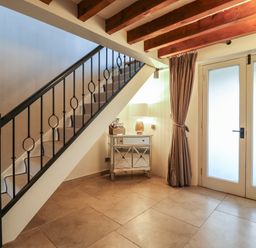 An entryway with a staircase railing a small mirrored cabinet with a lamp and frosted glass double doors at Bridge Barn in Sidestrand near Overstrand