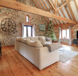 A living room with a beige sofa a Christmas tree a large wall clock a piano a television and wooden beams at Bridge Barn in Sidestrand near Overstrand