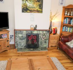 A living room with a wooden TV stand a fireplace with flowers a wooden bookshelf and a brown leather sofa at Lakeview Lodge in Knockmore County Mayo