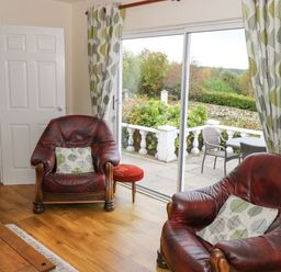 A sitting area with two leather armchairs and patterned curtains by sliding glass doors at Lakeview Lodge in Knockmore County Mayo
