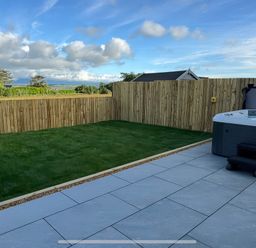 A garden with a hot tub and paved area at 15 Llys Tegeirian near Llangristiolus