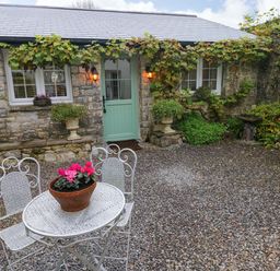 A stone house with a green door and windows with white frames a white metal table and chairs with a flower pot on the table at Little Cloud in Nash near Cowbridge
