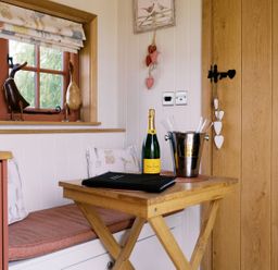 A corner with a table, champagne bottle, and decorative objects at Bonnie's Shepherds Hut at Shepherds Lodge Retreat and Wellness Bottesford near Redmile and Vale of Belvoir