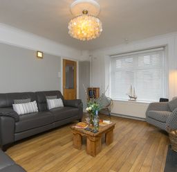 A living room with two gray sofas a small wooden table with wine glasses and snacks and a window with blinds at Captain's Walk in Newquay