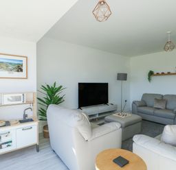 A living room with light colored sofas a television on a stand a small play kitchen and a plant at 6 Gwel Yr Wyddfa in Llanfaelog near Rhosneigr