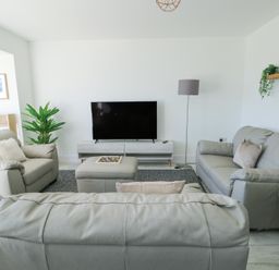 A living room with gray sofas a flat screen tv a floor lamp and a plant at 6 Gwel Yr Wyddfa in Llanfaelog near Rhosneigr