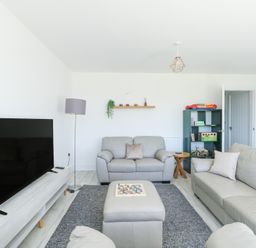 A living room with a television a gray rug a shelf with decor a floor lamp and beige sofas at 6 Gwel Yr Wyddfa in Llanfaelog near Rhosneigr