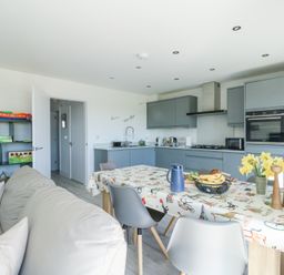 A kitchen and dining area with a table covered by a patterned tablecloth and a sofa nearby at 6 Gwel Yr Wyddfa in Llanfaelog near Rhosneigr