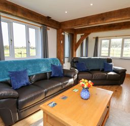 A living room with two black leather sofas a wooden coffee table and windows with grey curtains at Yr Adfa in Llangeitho near Tregaron